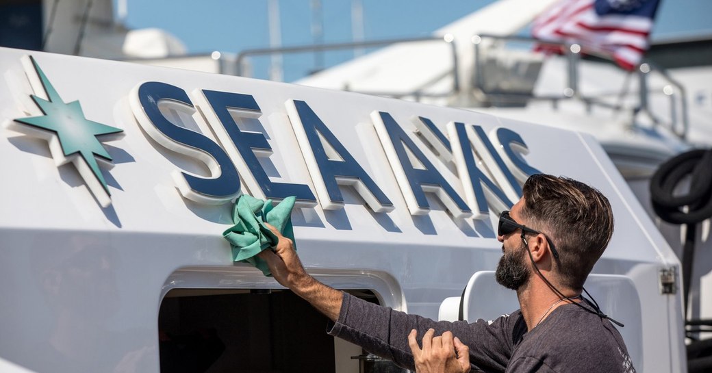 A crew member cleaning the aft deck and nameplate of charter yacht SEA AXIS at the Newport Charter Yacht Show