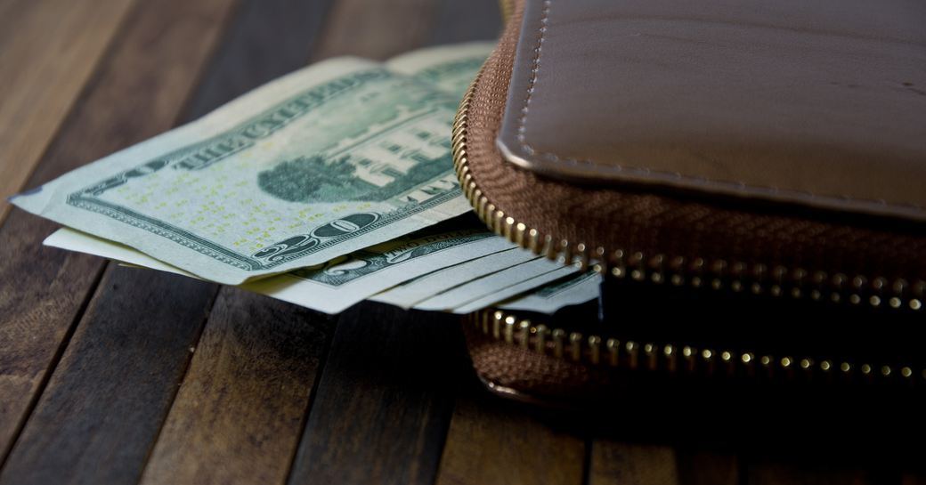 Dollar bills poking out of wallet on a wooden surface