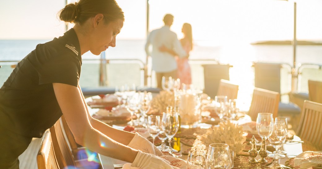 crew member sets the dining table on the upper deck aft of charter yacht Lady Joy 