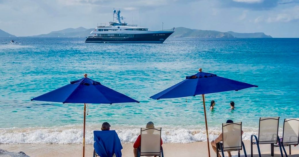 family sit on sandy beach looking at yacht on the horizon during yacht charter vacation in the bahamas