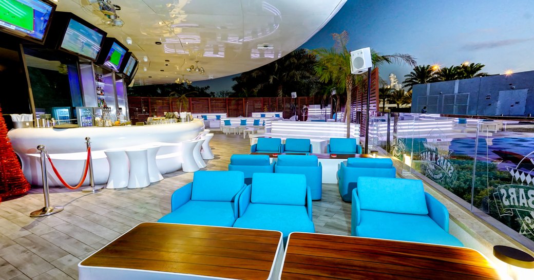 Outdoor terrace at Stars N Bars in Yas Marina, blue sofa seating and bar with television screens above 