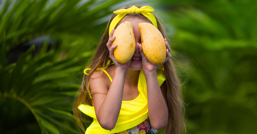 A girl masks her eyes with mangoes on Nevis Island in the Caribbean