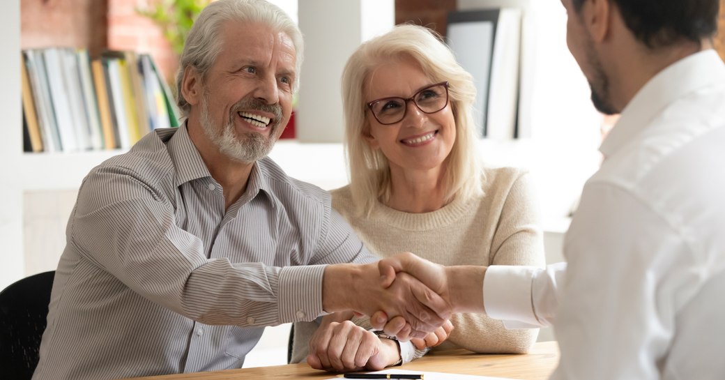 A middle-aged couple in a meeting with a professional man shaking hands