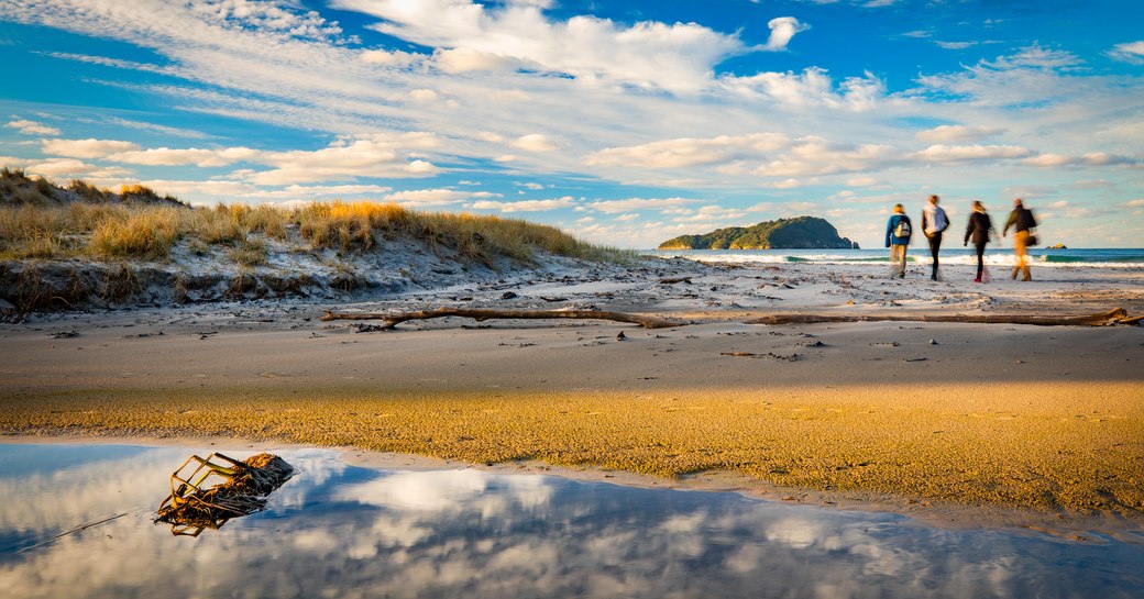 four travellers walk along Pauanui Beach, Coromandel Peninsula, New Zealand