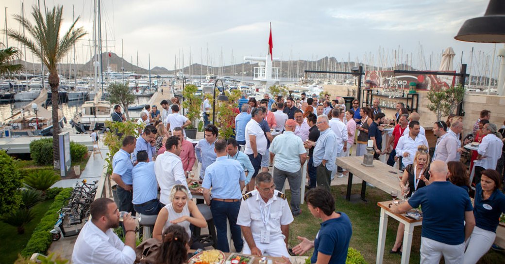 Visitors to the TYBA Charter Show sat outside enjoying lunch. Motor yachts and sail boats moored in background.