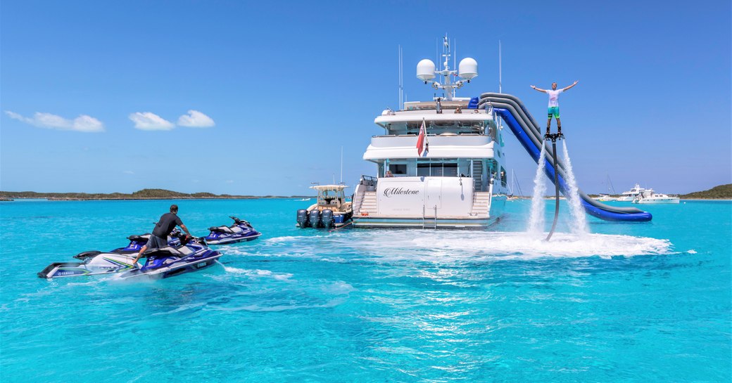 Superyacht MILESTONE at anchor, with charter guest using the Hoverboard and another guest on the Jet-Skis