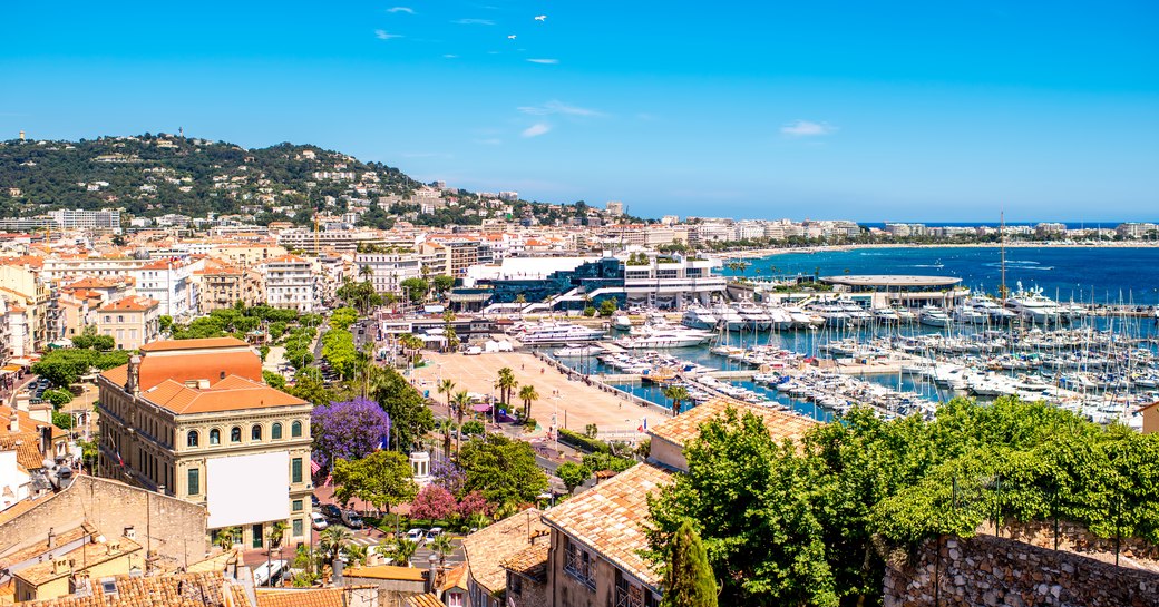 Elevated view of Cannes, buildings in foreground with marina down below. Many yachts berthed.