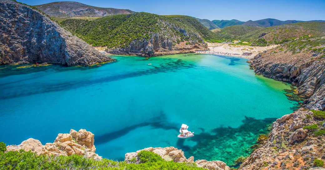 Bay in Sardinia, with bright blue water and white sand beach and Mediterranean terrain surrounding