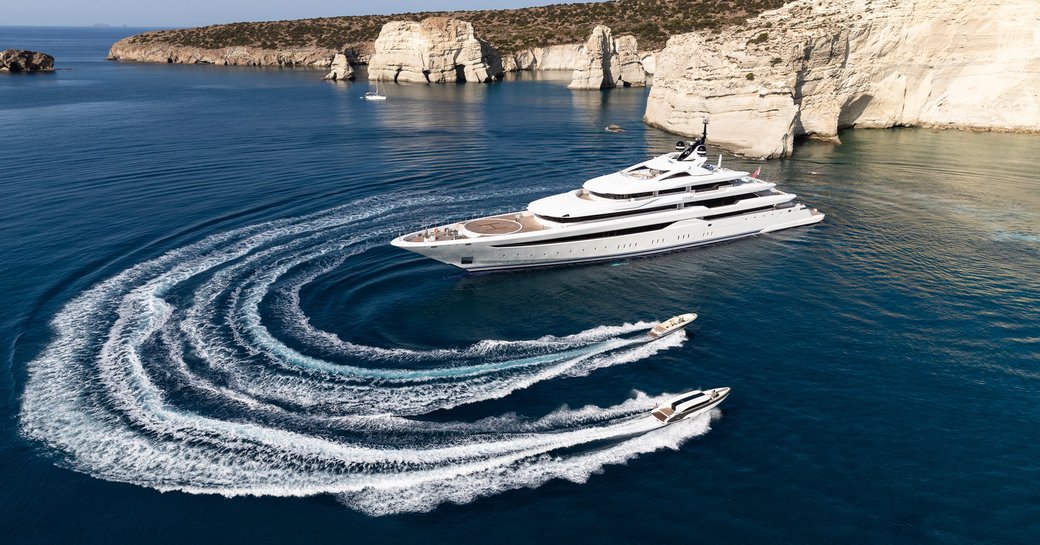 Superyacht O'PARI on water with dramatic coastline in background and two tenders nearby