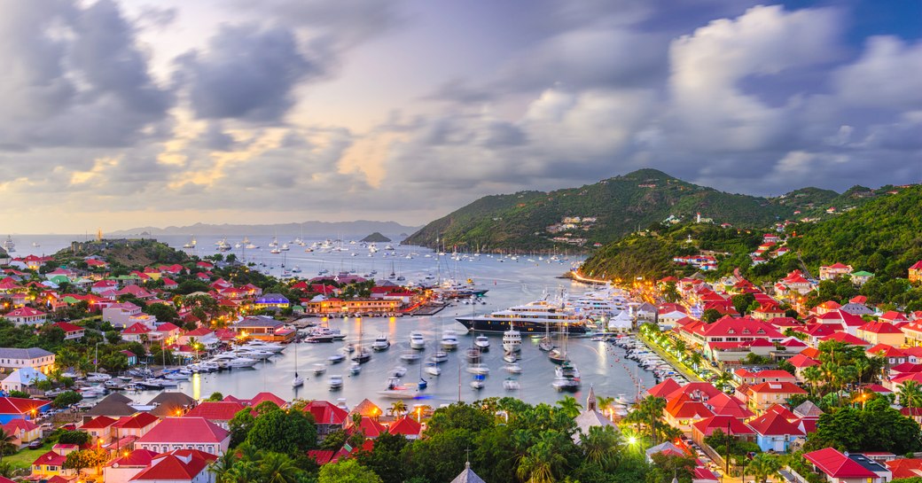 Panoramic view over St Barts in Caribbean showing hills, houses and harbour under a cloudy sky.