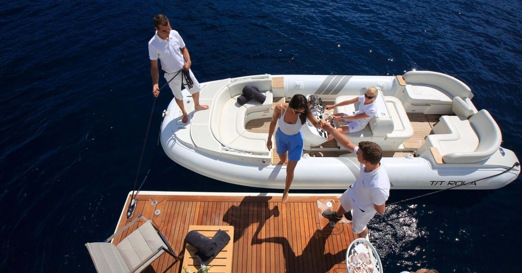 charter guest steps on board superyacht via swim platform, aerial view