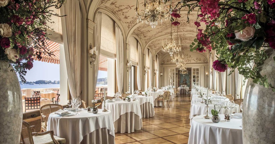 dining room of restaurant des Rois, La Réserve de Beaulieu,with white tables below arches overlooking the sea and red roses in vases