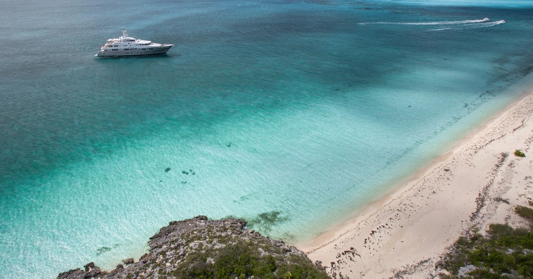 superyacht idles in the clear blue caribbean water opposite sandy beach