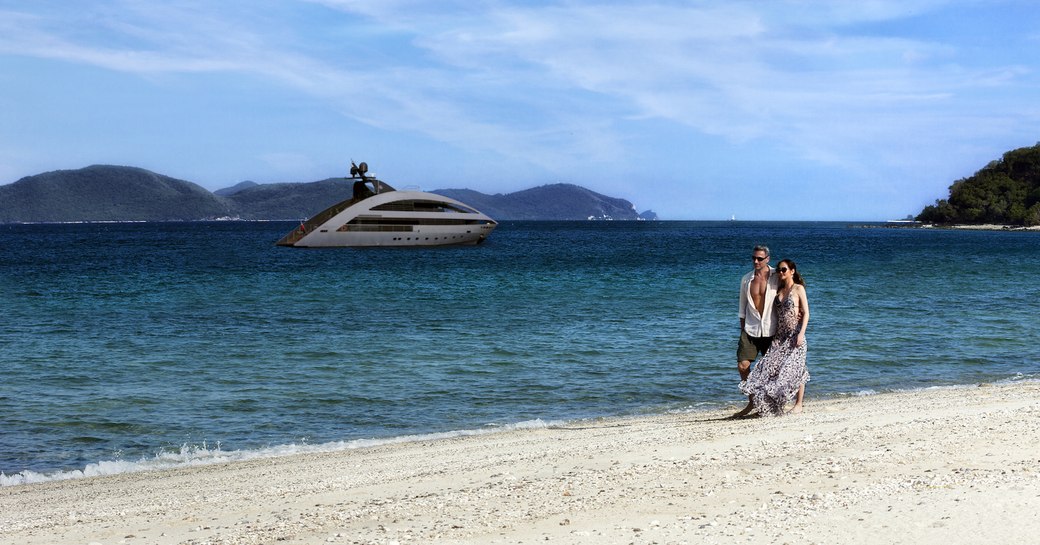 Couple on beach with motor yacht Ocean Emerald in distance.