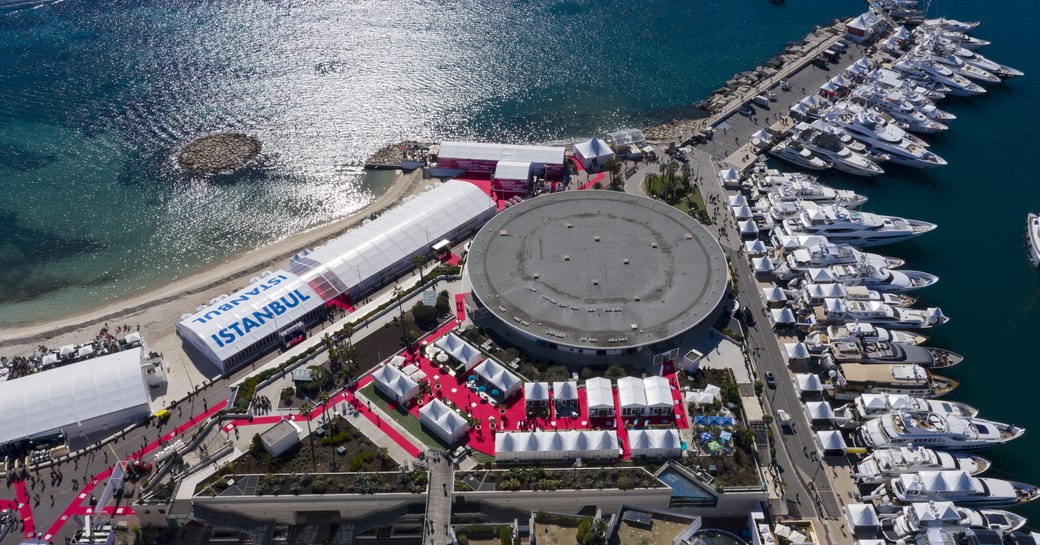 Aerial overview of MIPIM Cannes, many motoryachts moored in marina adjacent to exhibition building and tents.