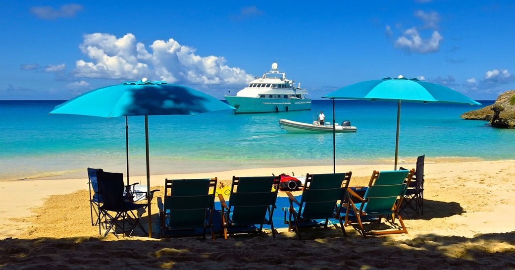 luxury yacht LIONSHARE anchors off the coast of a sandy beach with deck chairs 