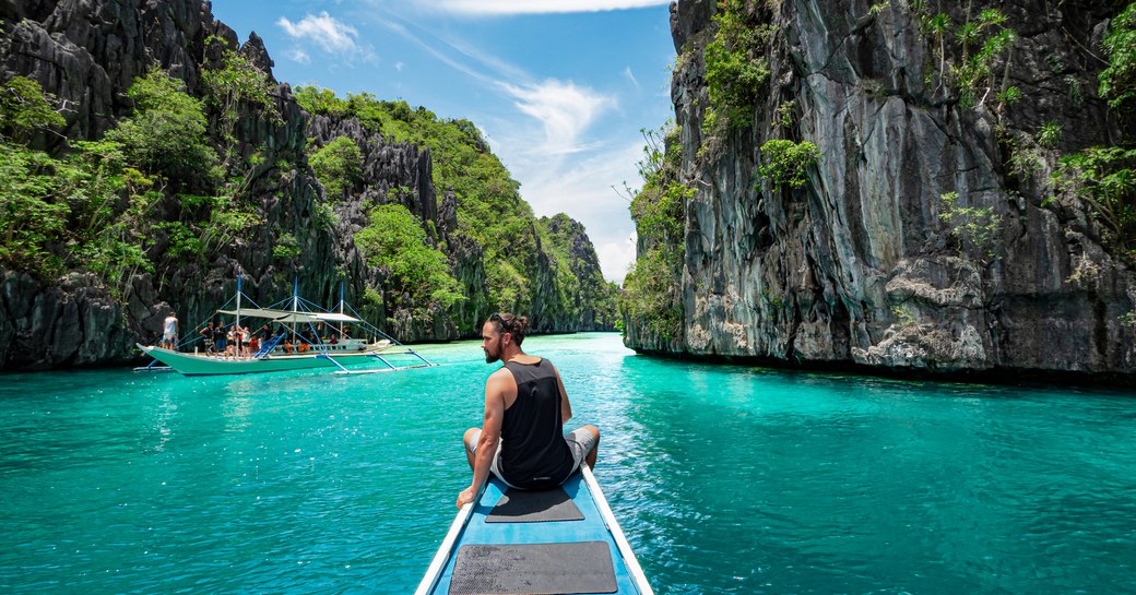 A man on the end of a longboat traveling through monolithic limestone rocks in the Philippines in Southeast Asia