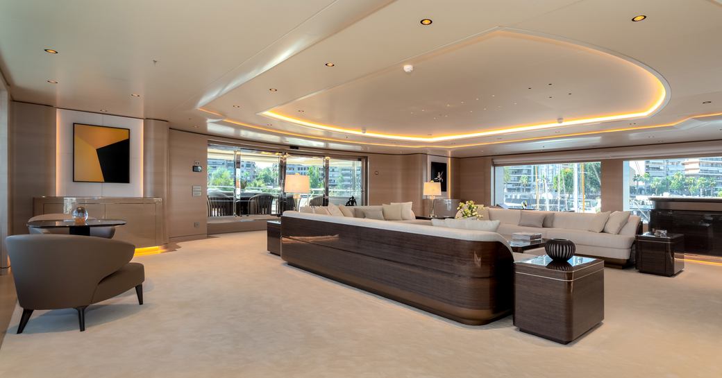 Large open plan room on superyacht O'PARI, three sofas visible on right and chair and small table on left with large windows all around