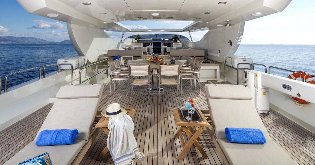 Upper deck of superyacht RINI with sun loungers in foreground and alfresco dining area beyond