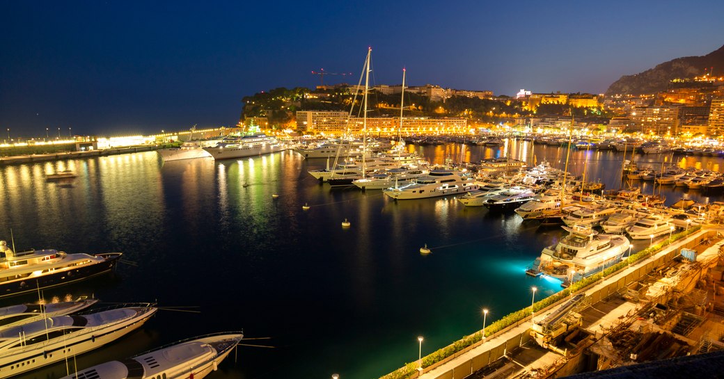 Port Hercule at the Monaco Yacht Show at dusk. Marina lit up with motor yachts berthed.