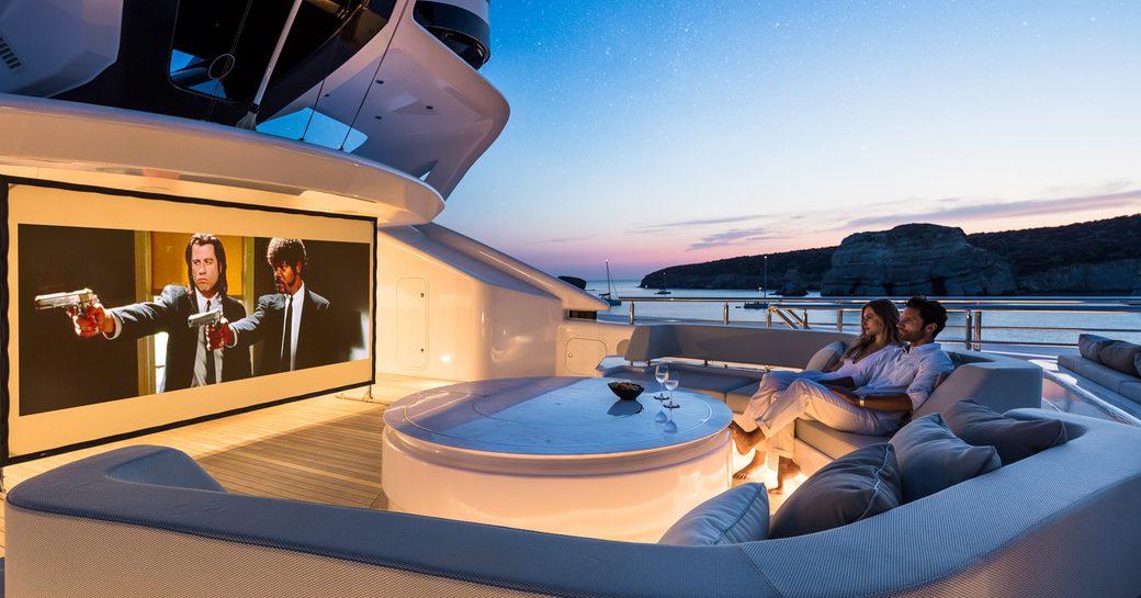 Couple sitting on deck of superyacht O'PARI watching film on large screen