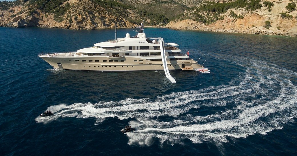 A superyacht with an inflatable slide attached and nearby Jetskis