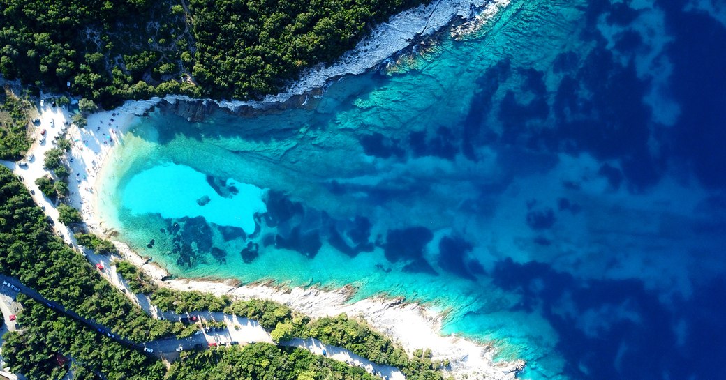 View from above of Caribbean coastline, with clear water and  white fringed beach surrounded by forest