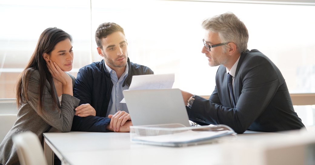 A couple in a meeting with a professional man pointing to a document