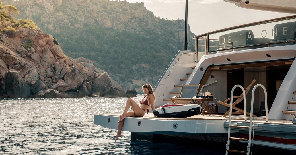 delta one large beach club with charter guest sitting off the back dangling feet in water 