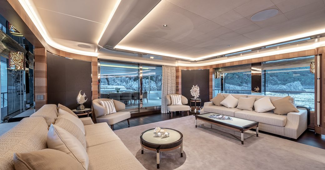 Main salon lounge area with plush cream seating and full height windows onboard charter yacht SUNRISE