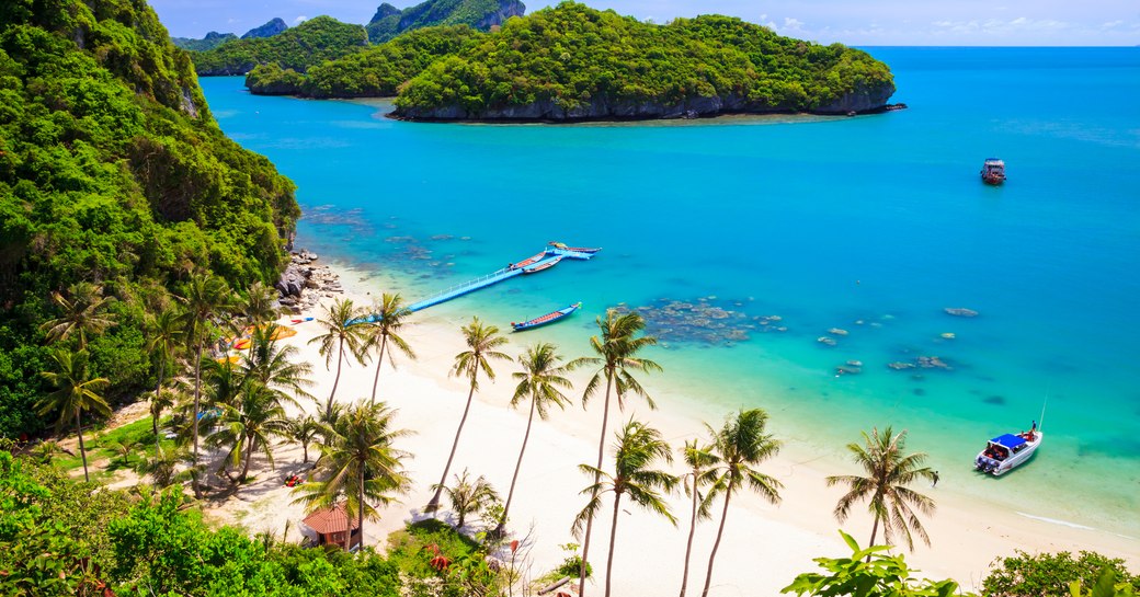 forested islands and a deserted white beach sit in green waters in thailand