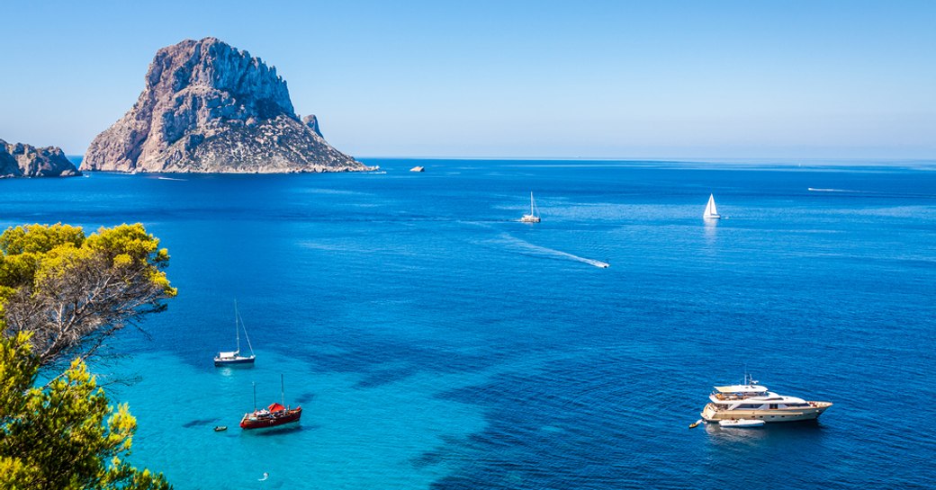 charter yachts bob along in the clear blue waters of ibiza, opposite the landmark of es vedra