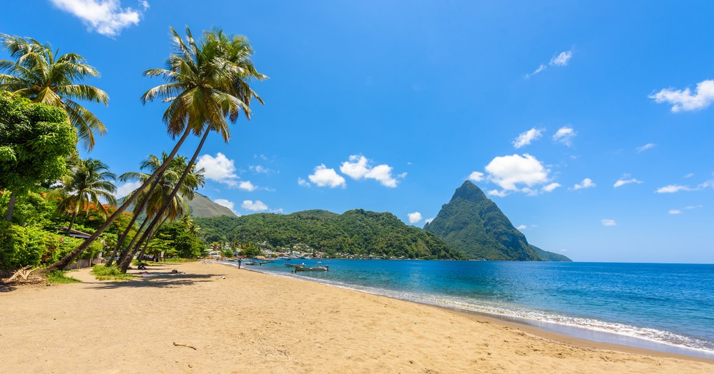 the island of antigua with a montenous background and soft sandy beach at the peak of Caribbean charter season