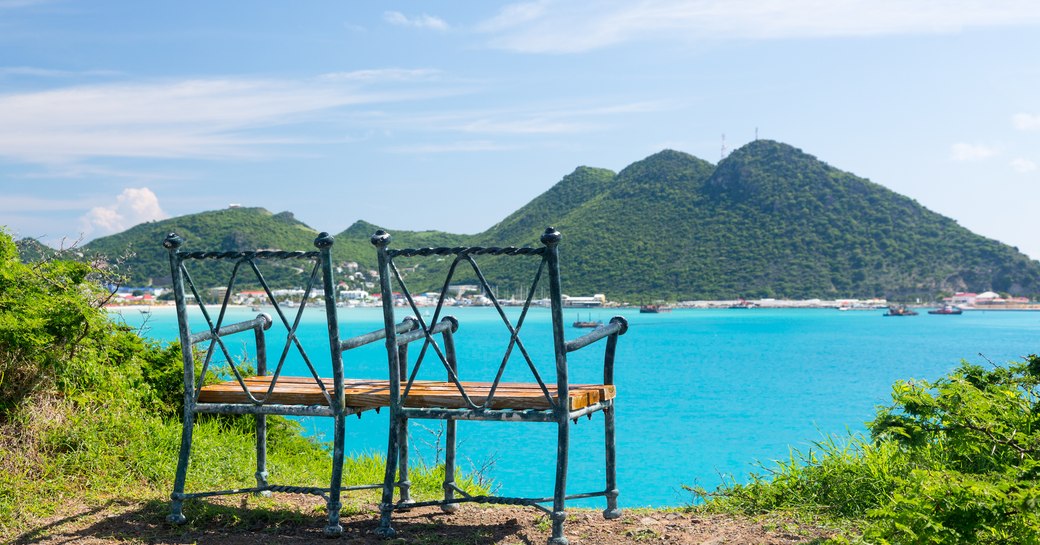 over the shoulder shot of two deck chairs looking out the Caribbean ocean and the mountainous rand that sits in the distance.