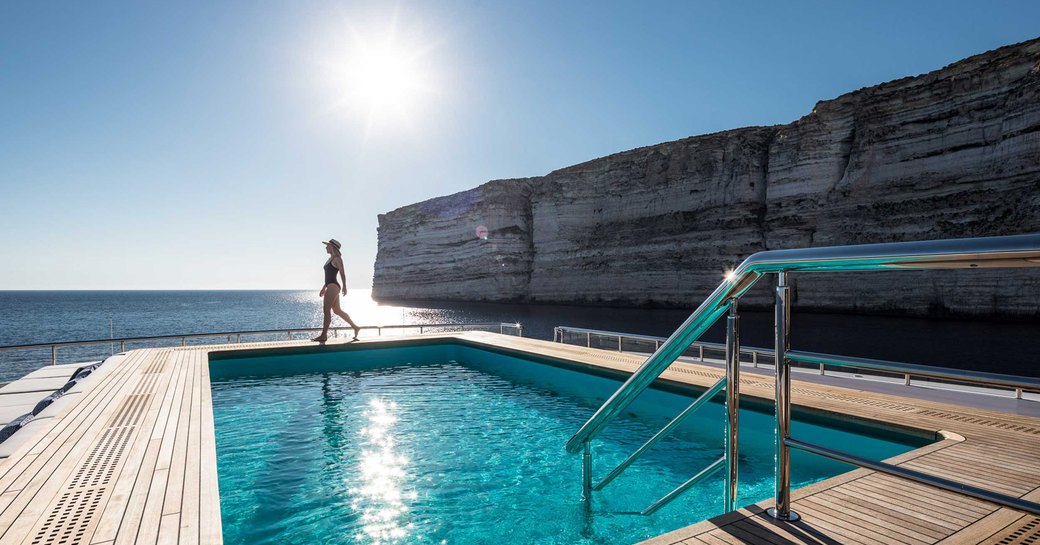 Pool on deck of Superyacht LANA with lady in swimsuit and coast in background