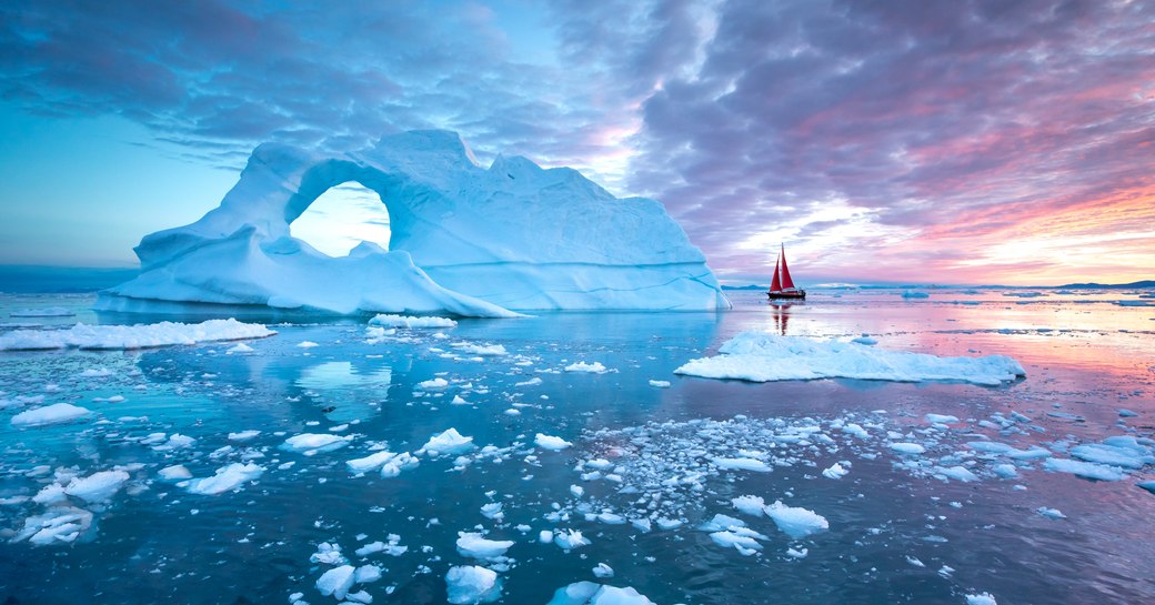 Little red sailboat cruising among floating icebergs in Disko Bay glacier during midnight sun season of polar summer in Greenland