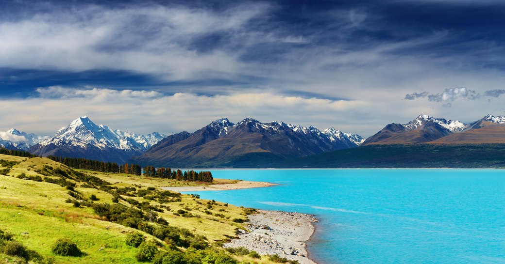 Mountainous landscape with lake and greenery in foreground and cloudy skies