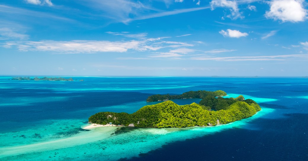 Aerial shot of jungle covered island in the South Pacific, with blue lagoons surrounding