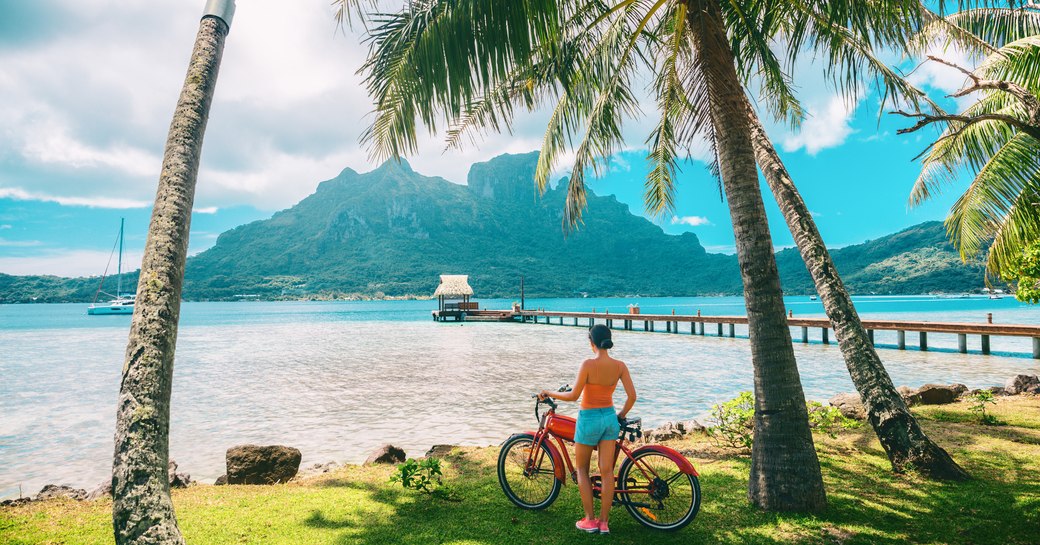 woman holding a bicycle looking out onto the stunning scenery and mountainous landscapes in Thaiti