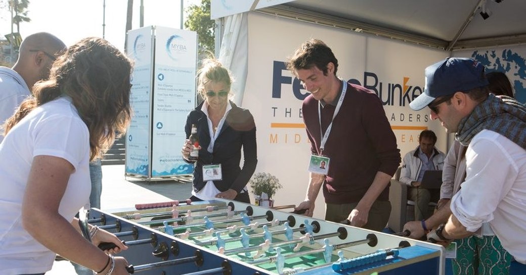 Exhibitors and visitors partaking in a table football match at MYBA event in Barcelona.