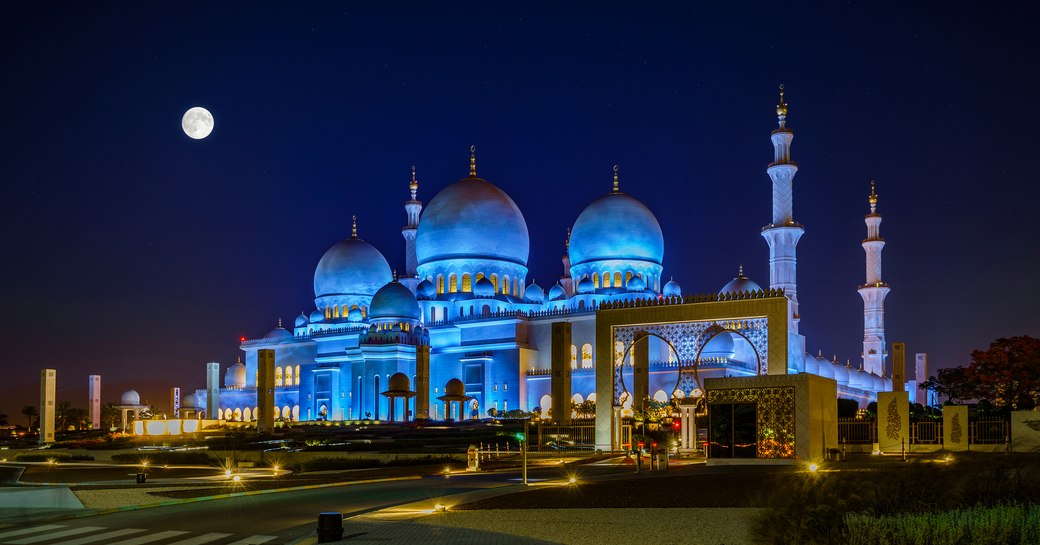 Sheikh Zayed Grand Mosque in Abu Dhabi lights up at night with a full moon in the sky above