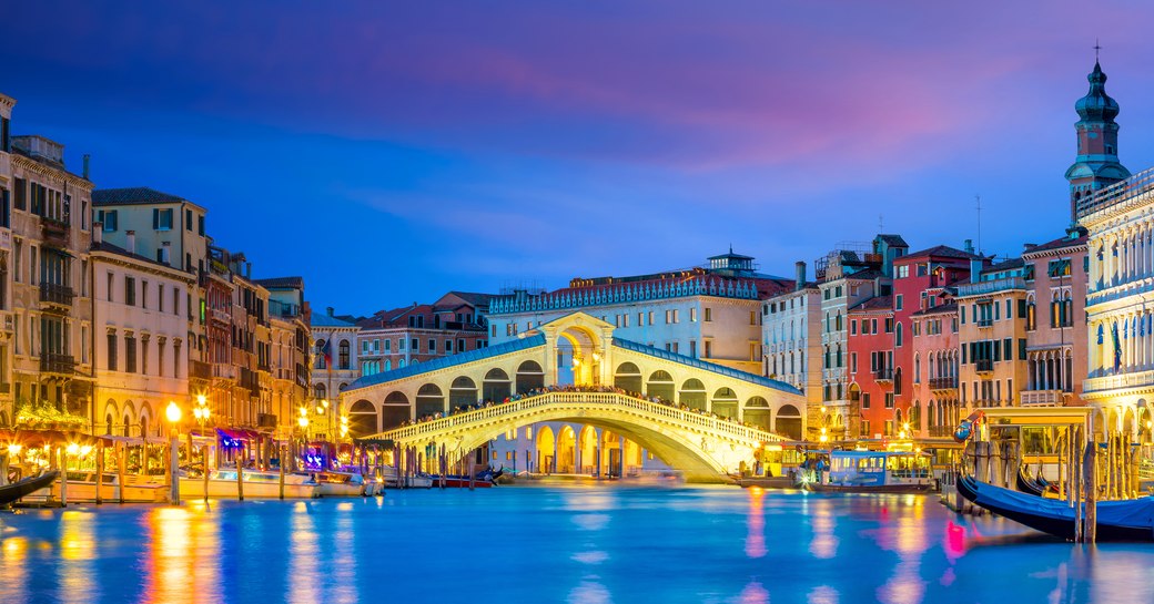 Picture taken from the centre of the grand canal, the rialto bridge in the background. Restaurants and shops line the streets at night in Venice