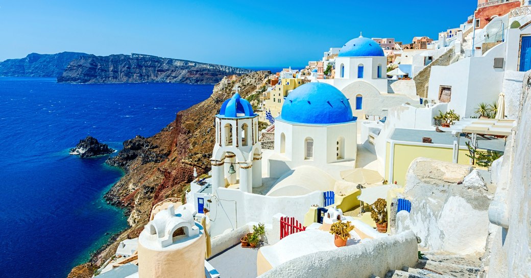 blue doomed buildings and white houses tumble down hillside in Santorini, Greece