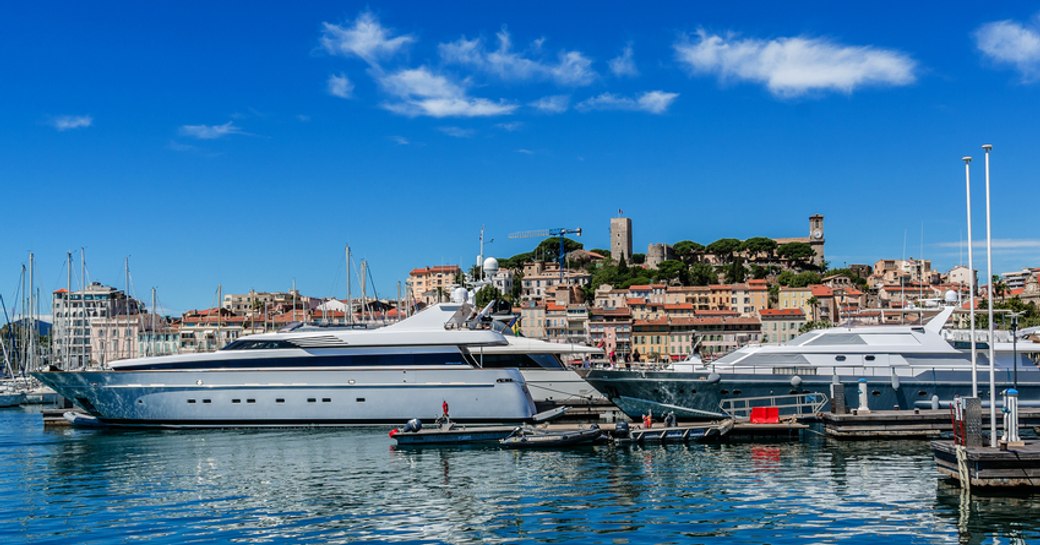 Superyachts moored in marina in front of Cannes, surrounded by sea and town of Cannes in background.