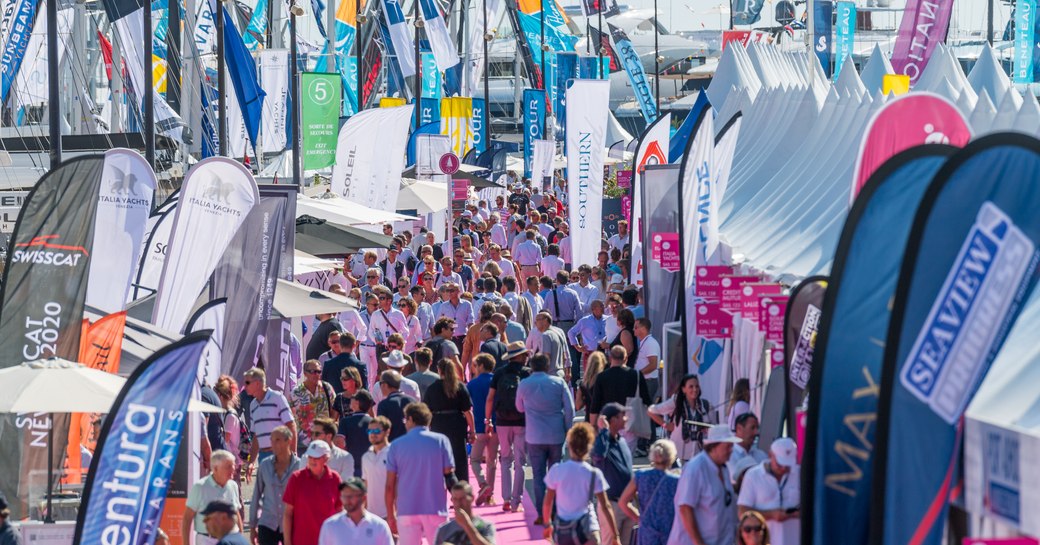 Visitors to Cannes Yachting Festival walking on red carpet looking at sailing boat displays on either side.