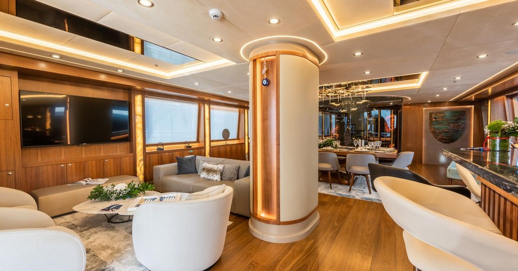 Main salon of sailing yacht ARESTEAS, with discreet lighting panels and warm wood with formal dining in background