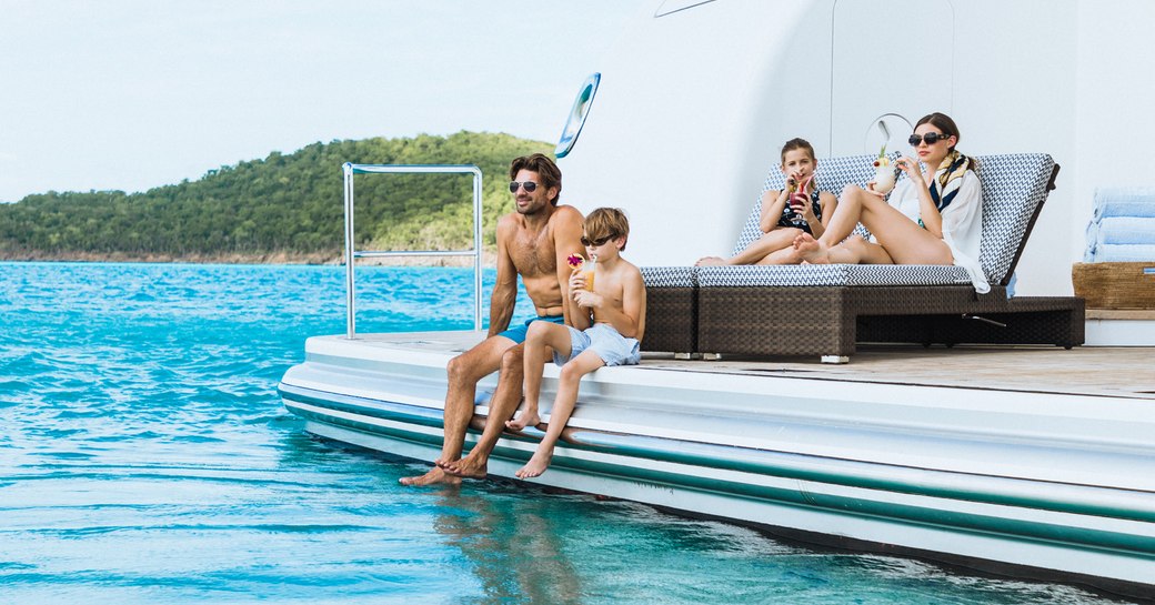Family sips drinks on beach club and swim platform of motor yacht TITANIA in the Maldives