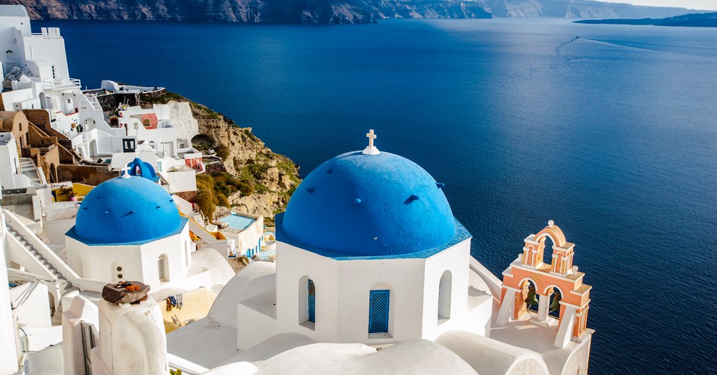 Blue chapels and white buildings in Greece, with sapphire sea inbackground