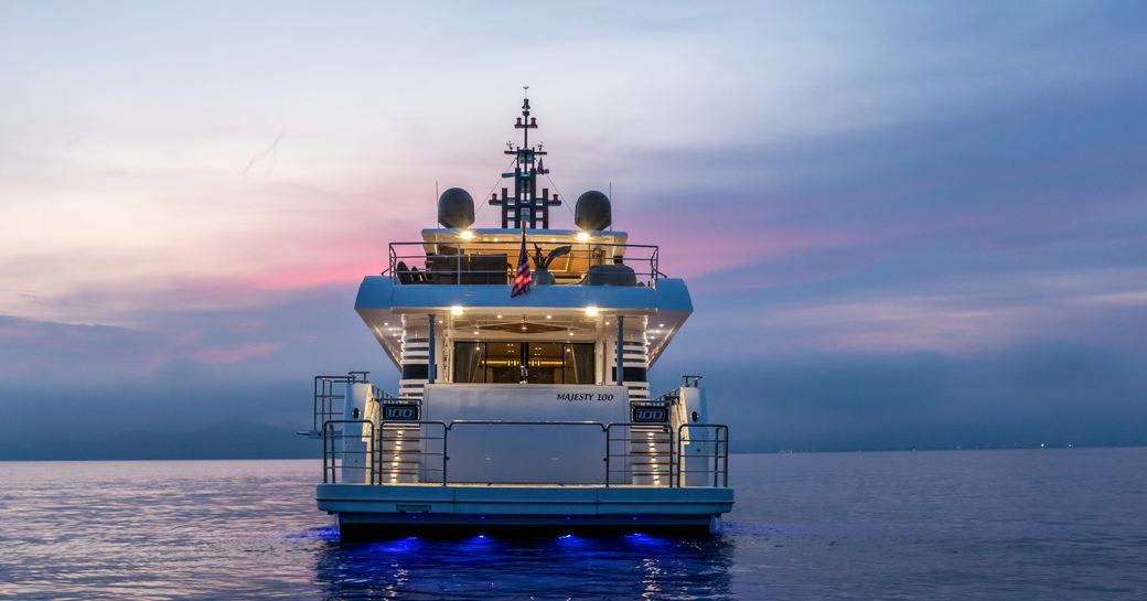 stern shot of majesty 100 yacht by gulf craft at sunset, with lights on deck switched on