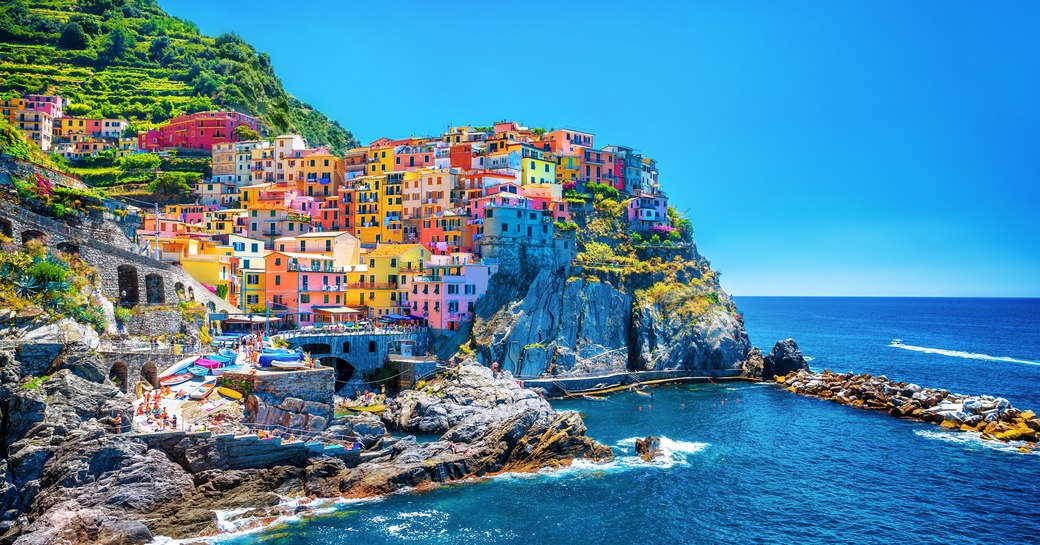 candy coloured houses stacked atop each other on a clif by a coastal town in the amalfi coast